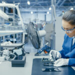 Young Female Blue and White Work Coat is Using Plier to Assemble Printed Circuit Board for Smartphone. Electronics Factory Workers in a High Tech Factory Facility.