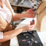 Cropped photo of a handcrafter examining the gemstones on a new pendant hanging on the display bust