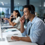 Shot of a young man using a headset and computer in a modern office.