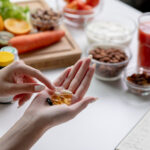 Woman professional nutritionist checking dietary supplements in hand, surrounded by a variety of fruits, nuts, vegetables, and dietary supplements on the table